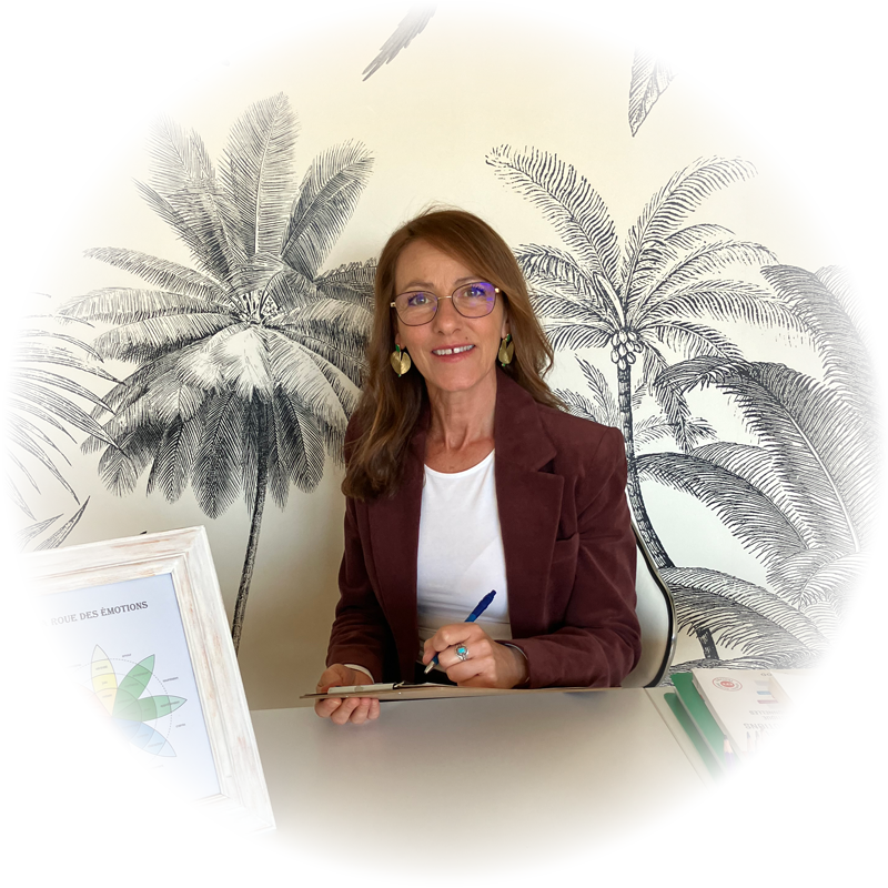 Photo de Sophie Ianni, Thérapeute Cognitive et Comportementale - Praticienne en Intelligence Émotionnelle, assise à son bureau professionnelle, prenant des notes, devant un mur tapissé avec des palmiers